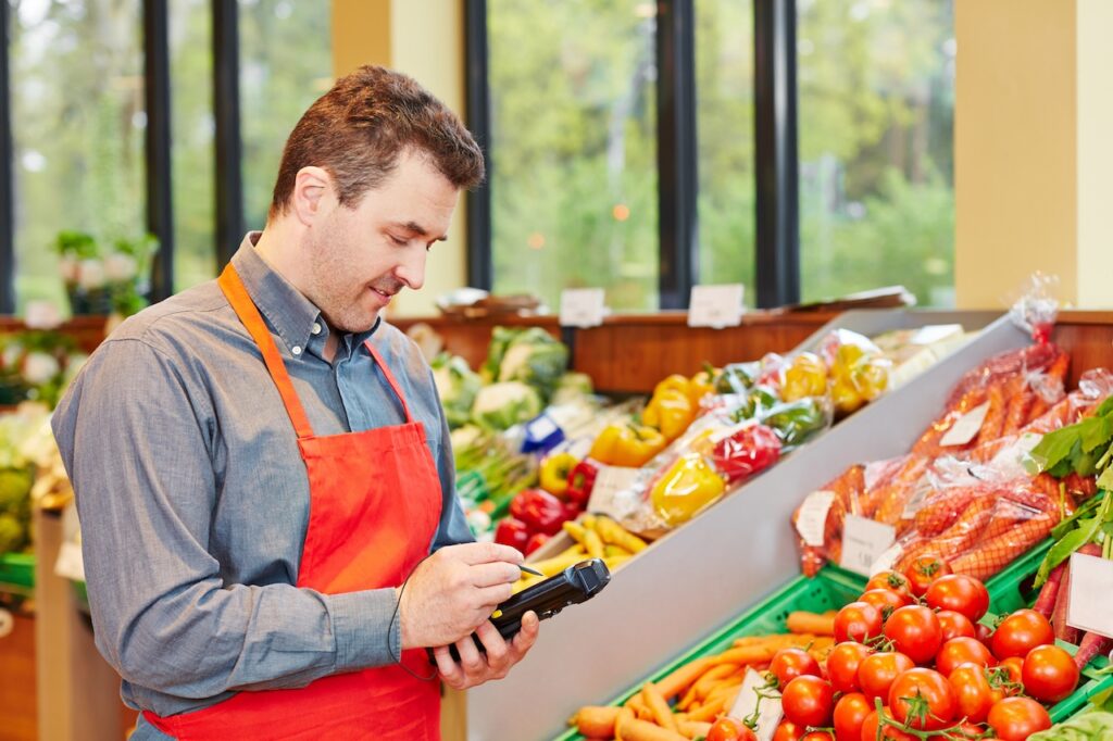 Ein Supermarktmitarbeiter nutzt ein MDE-Gerät zur Bestandsaufnahme und Warenerfassung im Obst- und Gemüsesortiment.