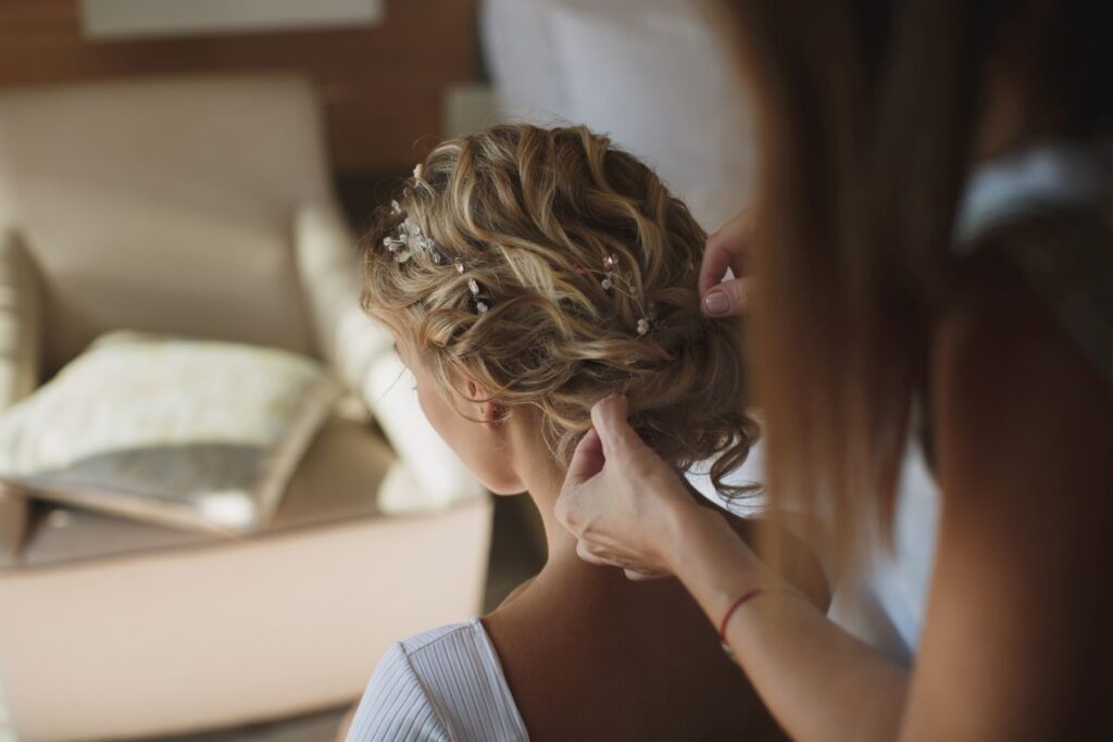 Stylistin richtet eine Hochsteckfrisur bei einer Frau mit blondem Haar, Clip In Extensions sorgen fuer Volumen und Form